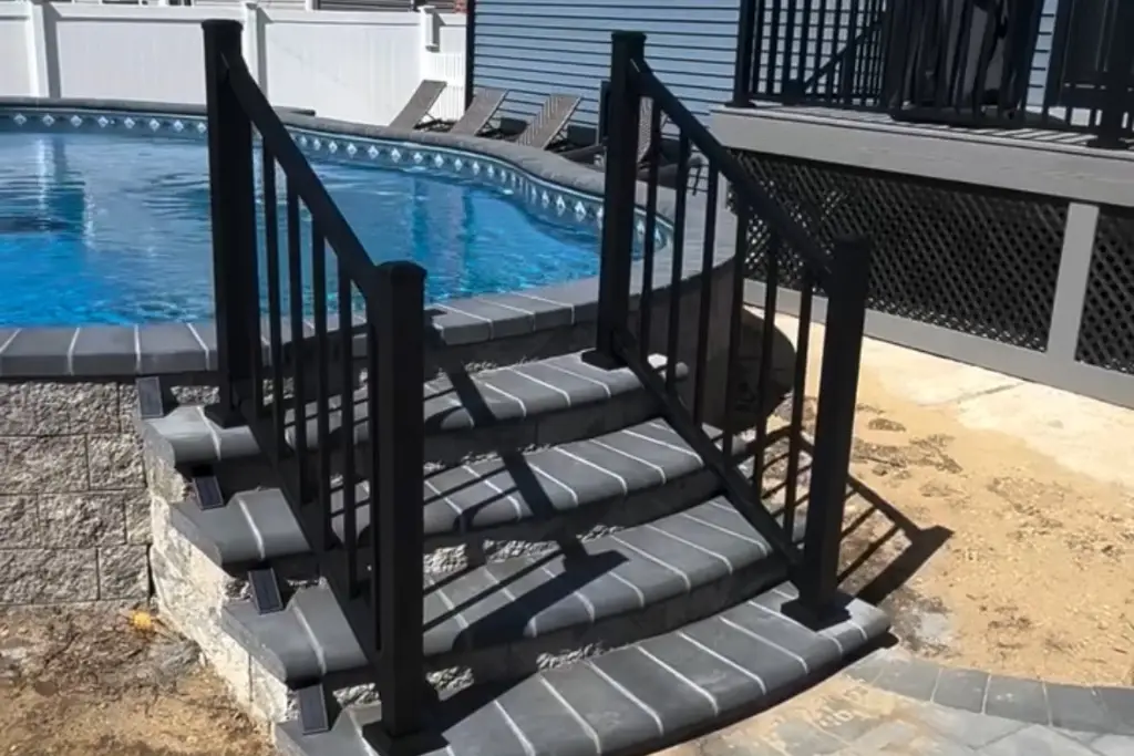 Black aluminum railing installed on deck stairs with gray stone steps, leading down to a pool area for added safety and modern appeal.